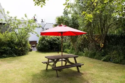 a picnic table with a red umbrella in a yard at Cornish Cottage St Agnes free parking and garden in St. Agnes