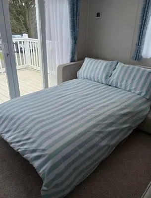 a bed with a blue and white striped blanket at Cosy three bedroom holiday home in Parkdean Newquay in Newquay