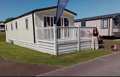 a woman standing in front of a trailer with a dog at Cosy three bedroom holiday home in Parkdean Newquay in Newquay