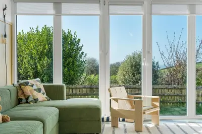 a living room with a couch and a chair and large windows at Beach Life Cabin Vibes Ocean Views nr Bude in Bude