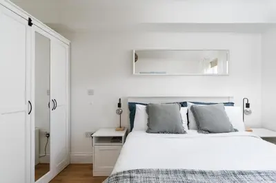 a white bedroom with a white bed and a mirror at Stylish Apartment Garden with Beautiful Sea Views in Newquay