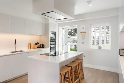a white kitchen with a counter and stools at Contemporary Townhouse with Sea Views & Parking in Newquay