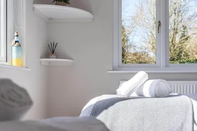 a white room with a bed with a table and two windows at Stunning House with Estuary Views Padstow in Padstow