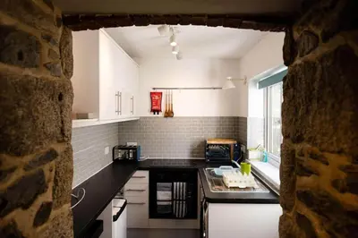 a kitchen with white cabinets and a black counter top at Smugglers Cottage in Penryn Nr Falmouth in Penryn