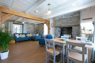 a living room with a table and a stone fireplace at Homely Cottage with Sun Terrace Short Walk to Beach in Porthleven