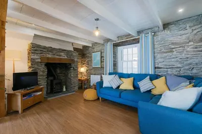 a living room with a blue couch and a stone wall at Homely Cottage with Sun Terrace Short Walk to Beach in Porthleven