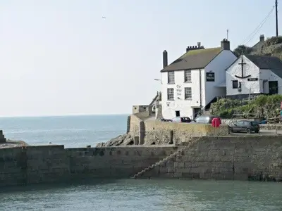 a white house on a cliff next to the water at Homely Cottage with Sun Terrace Short Walk to Beach in Porthleven