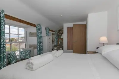 a bedroom with a large white bed and a window at Homely Cottage with Sun Terrace Short Walk to Beach in Porthleven