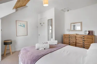 a white bedroom with a bed and a dresser at Beach-Style Flat 2 Min Walk to Tolcarne Beach in Newquay