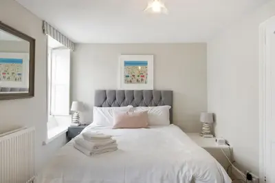 a white bedroom with a large white bed with a pink pillow at 18th Century Cottage with Garden Central Newquay in Newquay