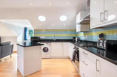 a kitchen with white cabinets and a black counter top at Spacious Flat A Few Mins Walk to Carlyon Bay Beach in Carlyon Bay