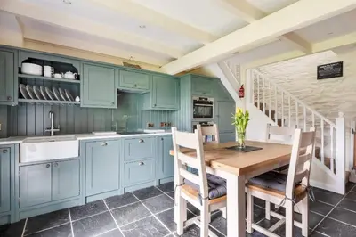 a kitchen with blue cabinets and a wooden table and chairs at 2 Bedroom Cottage Close to Perranporth Beach in Roche