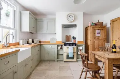 a kitchen with white cabinets and a wooden table at Gin O'Clock Mevagissey Level Walk to Harbour in Mevagissey