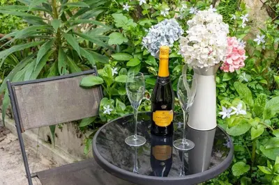 two bottles of wine and glasses on a table with flowers at Gin O'Clock Mevagissey Level Walk to Harbour in Mevagissey