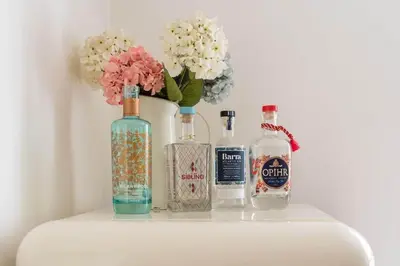a shelf with three bottles and a vase with flowers at Gin O'Clock Mevagissey Level Walk to Harbour in Mevagissey