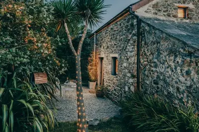 a palm tree next to a stone building with a string of lights at Romantic Converted Barn Perfect St Agnes Location in St. Agnes