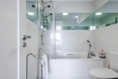 a white bathroom with a shower and a toilet at Bright Flat with Estuary Views & Parking Falmouth in Falmouth