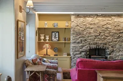 a living room with two chairs and a stone fireplace at 19th Century Cottage & Garden Private Parking in Perranporth