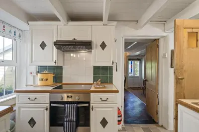 a kitchen with white cabinets and a stove top oven at 19th Century Cottage & Garden Private Parking in Perranporth