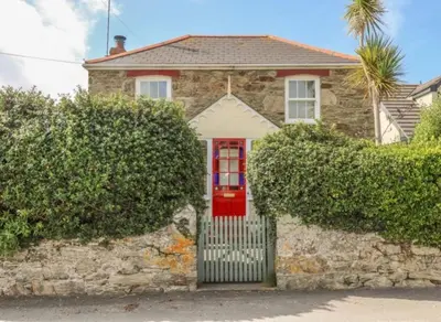 a red door on a stone house with bushes at 19th Century Cottage & Garden Private Parking in Perranporth