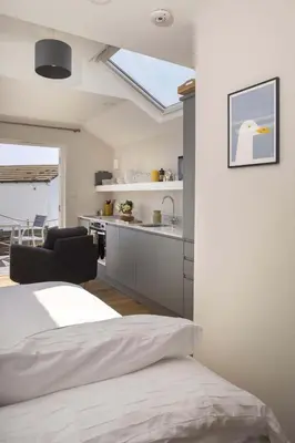 a bedroom with a bed and a kitchen with a window at Cottage & Boatshed in Gorran Haven Private Parking in Gorran Haven