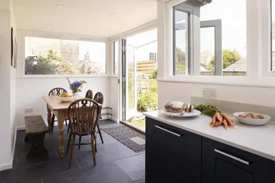 a kitchen with a table and a dining room with windows at Cottage & Boatshed in Gorran Haven Private Parking in Gorran Haven