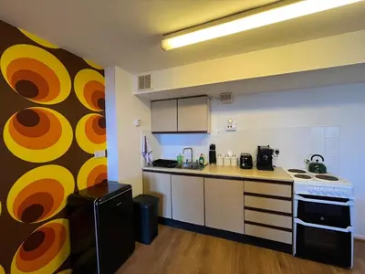 a kitchen with white cabinets and a yellow and orange wall at Retro Ocean View Pad by Fistral Beach in Newquay