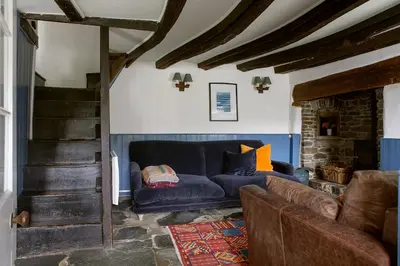 a living room with a blue couch and a staircase at Old Cottage 1 min from the sea! Crackington Haven in Crackington Haven