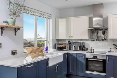 a kitchen with blue cabinets and a large window at Parkland Place - Spacious Newquay family holiday home, parking, log burner, dog friendly in Saint Columb Minor