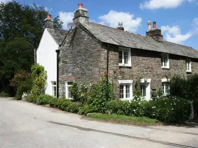 an old brick house with flowers in front of it at Hollyhocks Cottage surrounded by beautiful Cornish countryside. in Helland