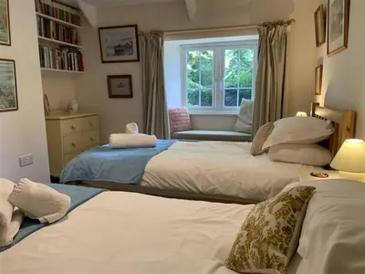 two beds in a bedroom with a window at Hollyhocks Cottage surrounded by beautiful Cornish countryside. in Helland