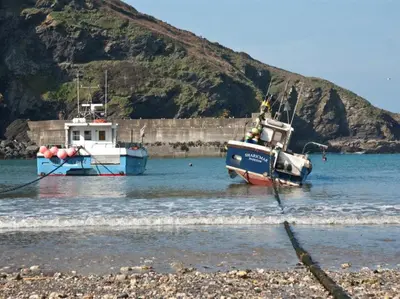 two boats are docked in the water near a mountain at Harbour Loft Port Isaac harbour beach views in Port Isaac