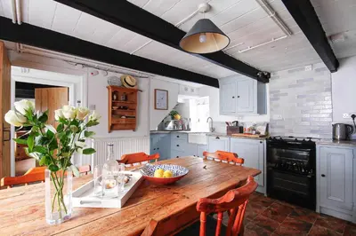a kitchen with a wooden table with a vase of flowers at Crotchet Cottage near sandy beach at Porthbeor in Saint Anthony