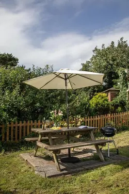 a picnic table with an umbrella and a grill at Crotchet Cottage near sandy beach at Porthbeor in Saint Anthony