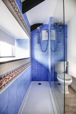 a blue tiled bathroom with a shower and a toilet at Crotchet Cottage near sandy beach at Porthbeor in Saint Anthony