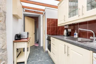 a kitchen with white cabinets and a sink at Tinners Forge a pretty cottage near Mevagissey in St Austell