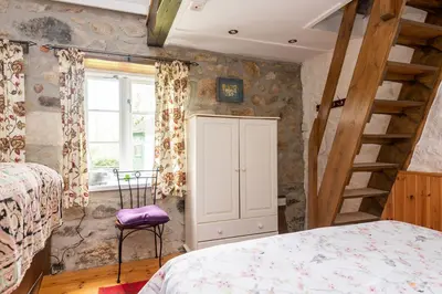 a bedroom with a bed and a ladder and a window at Tinners Forge a pretty cottage near Mevagissey in St Austell