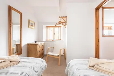 a bedroom with two beds and a chair and a dresser at Fernleigh Cottage near the North Cornish beaches in Saint Mabyn