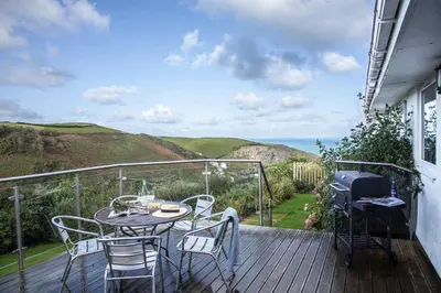 a table and chairs on a deck with a view of the ocean at Silvershell lovely views across Port Isaac in Port Isaac