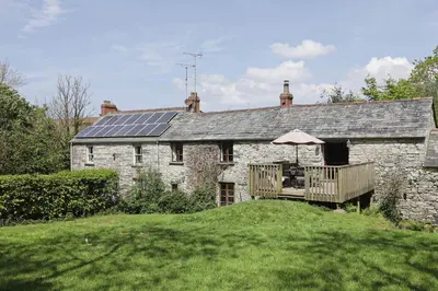 an old stone house with a deck with an umbrella at The Barn in Camelford