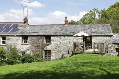 an old stone house with a deck with an umbrella at The Barn in Camelford
