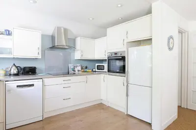 a white kitchen with white cabinets and appliances at Sail Loft — A quiet St Mawes gem in Saint Mawes