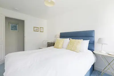 a bedroom with a large white bed with a blue headboard at Sail Loft — A quiet St Mawes gem in Saint Mawes