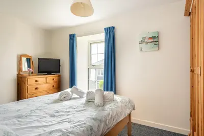 a bedroom with a bed with blue curtains and a window at Rosemary Cottage Edmonton set in the countryside in Wadebridge