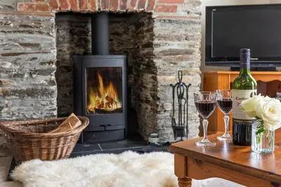 a living room with a fireplace and a table with wine glasses at Rosemary Cottage Edmonton set in the countryside in Wadebridge