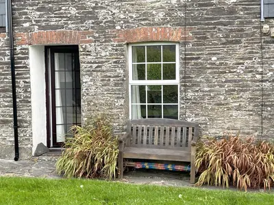 a wooden bench sitting in front of a brick building at Rosemary Cottage Edmonton set in the countryside in Wadebridge