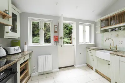 a kitchen with white cabinets and a sink and windows at Well Court is a fabulous cottage with wonderful views set in the heart of Polruan village in Fowey