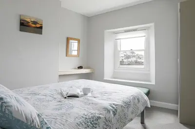 a white bedroom with a bed and a window at Well Court is a fabulous cottage with wonderful views set in the heart of Polruan village in Fowey