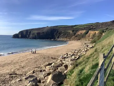 two people walking on a beach next to the ocean at Hideaway Barn in Germoe