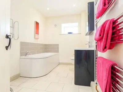 a bathroom with a tub and a toilet and pink towels at Hideaway Barn in Germoe